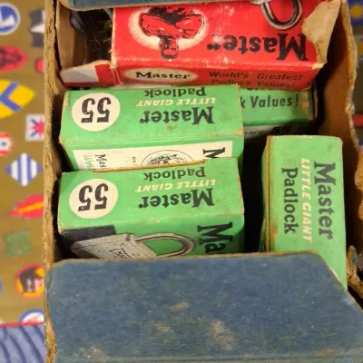 Vintage box filled with boxed Master Lock padlocks, including Little Giant No. 55 models, showing original colorful packaging.