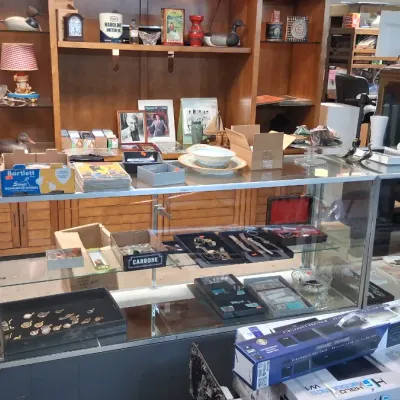 Glass display cases filled with assorted estate sale items, including jewelry, watches, collectibles, and home electronics, in front of...