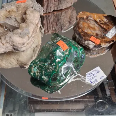 Collection of mineral specimens and petrified wood displayed on a mirrored tray, including a polished green malachite and chrysocolla...