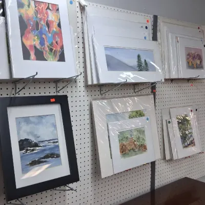 Collection of framed and matted art prints and watercolor paintings displayed on a pegboard wall.