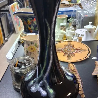 Tall black art pottery vase featuring a bulbous base and a drip glaze accent in iridescent silver and green tones.