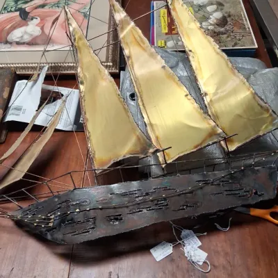 Vintage mid-century brutalist welded metal and brass sailboat wall sculpture resting on a wooden tabletop.