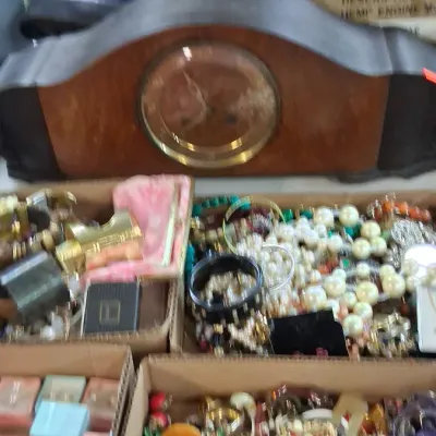 Vintage wooden mantel clock displayed above several cardboard boxes filled with assorted costume jewelry and small accessories.