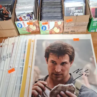 Collection of sports trading cards in protective sleeves and storage boxes alongside signed celebrity and pop culture photos in binder...