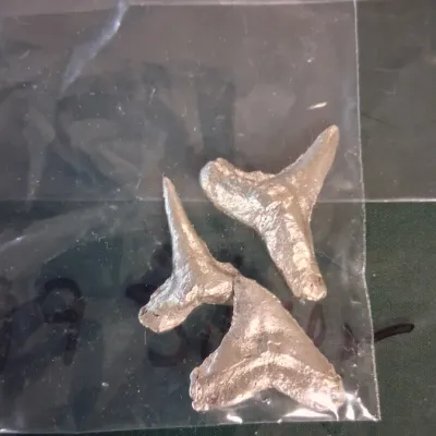 Set of three 999 silver hand cast metal shark tooth charms or pendants contained in a plastic bag.