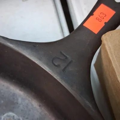 Vintage cast iron skillet featuring a size number 12 stamp on the top handle base, showing minor surface wear and seasoning.