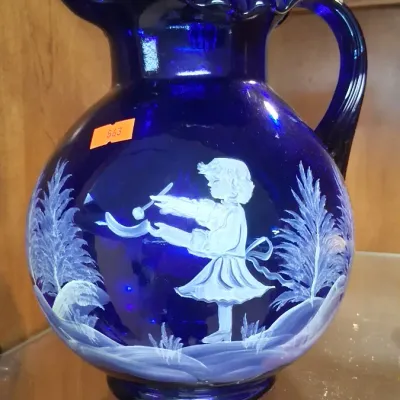 Cobalt blue glass Mary Gregory style pitcher with a ruffled rim and hand-painted white enamel scene depicting a young girl outdoors.