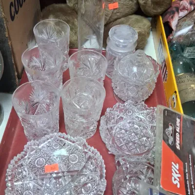 Collection of clear cut glass glassware including starburst pattern tumblers, a tall cylinder vase, candy dishes, and small bowls set on...