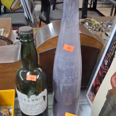Vintage Black & White blended Scotch whisky bottle alongside a tall, slender lavender glass bottle with a cork stopper.