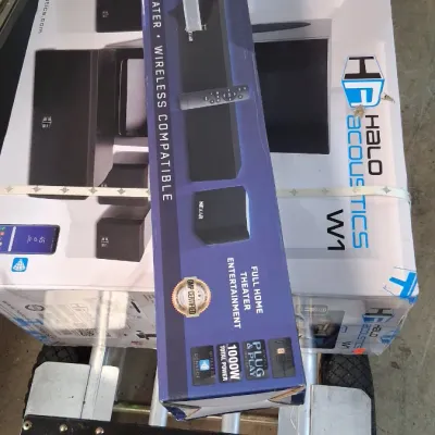 Boxed Halo Acoustics W1 home theater system resting on a hand truck next to a soundbar box.