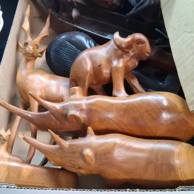 Cardboard box packed with hand-carved wooden African animal figures, including rhinos, a water buffalo, and an antelope, alongside dark...