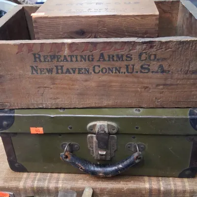 Vintage Winchester Repeating Arms Co. wooden crate stacked atop a green military-style trunk, accompanied by a smaller wooden box and...