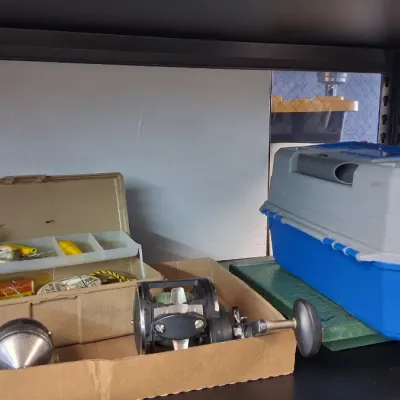Collection of fishing gear, featuring a beige plastic tackle box with contents, fishing reels, and a large blue and gray Plano tackle...