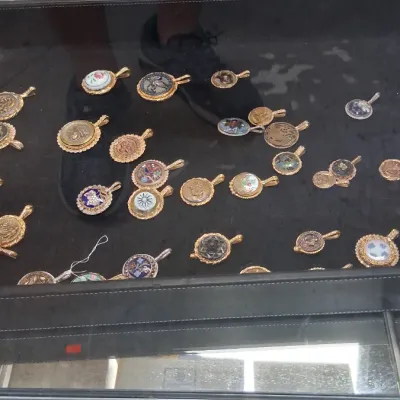 Collection of vintage micro mosaic and porcelain pendants displayed inside a glass showcase tray.