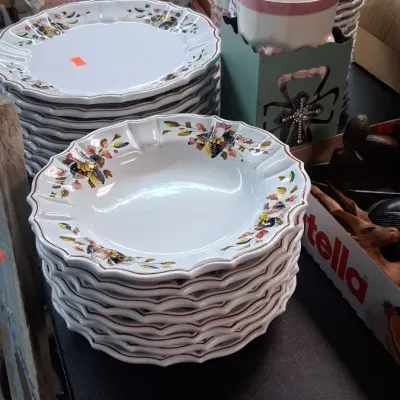 Stacks of floral pattern ceramic dinnerware and bowls on display alongside porcelain figurines and collectible dolls.