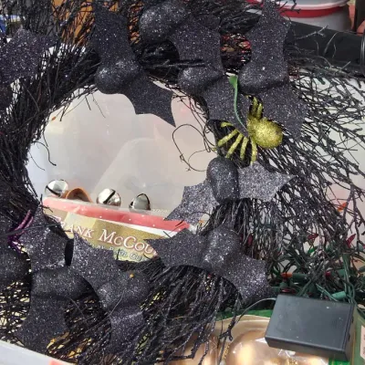 Black twig Halloween wreath decorated with glittery bats and a gold spider, resting in a storage bin alongside holiday decorations.