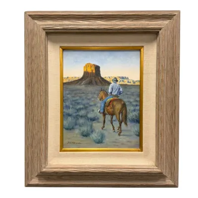 Sale Photo Thumbnail #47: Framed Western oil painting depicting a cowboy on horseback riding toward a mesa, housed in a textured wood frame with a linen fillet.