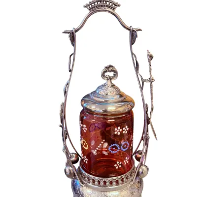 Sale Photo Thumbnail #54: Victorian silver-plated pickle castor featuring a hand-painted enamel floral amber glass jar, an ornate silver lid, and a decorative caddy frame with pickle tongs.