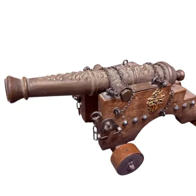 Sale Photo Thumbnail #18: Miniature brass and wood model cannon, featuring an embossed metal barrel, decorative crest on the wooden carriage, and metal chain details.