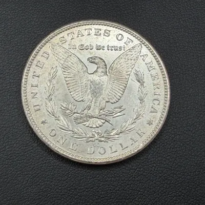 Sale Photo Thumbnail #73: Reverse side of a US Morgan silver dollar coin with CC Carson City mint mark, featuring an eagle design with outstretched wings.
