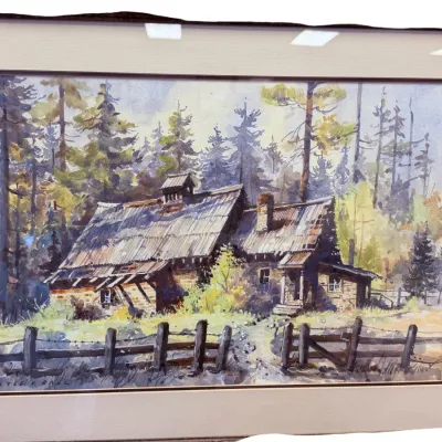 Sale Photo Thumbnail #58: Framed watercolor painting by Lyle V. Ball depicting a rustic wooden cabin surrounded by pine trees, presented in a wide beige mat and wooden frame.