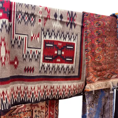 Sale Photo Thumbnail #36: Collection of woven textiles and rugs displayed on a rack, including a Southwestern Navajo-style flatweave rug and an intricate Persian runner.