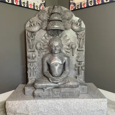 Sale Photo Thumbnail #17: Intricately carved stone stele featuring a seated Jain Tirthankara figure, resting on a thick rectangular stone plinth.