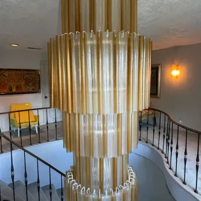 Sale Photo Thumbnail #15: Large multi-tier vintage Murano-style glass tube chandelier hanging over a stairwell, featuring alternating clear and gold-toned textured glass elements.