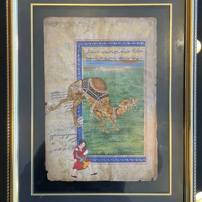 Sale Photo Thumbnail #43: Framed Indo-Persian miniature painting depicting a composite camel made of human and animal figures led by a attendant, rendered on manuscript paper with illuminated floral borders.