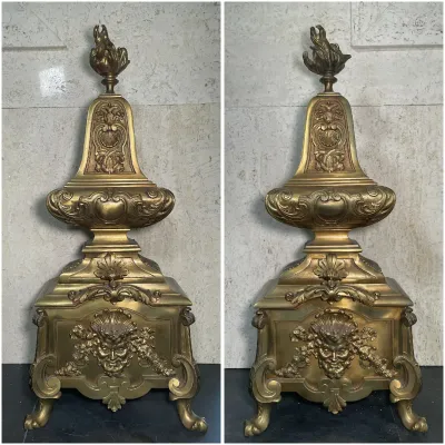 Sale Photo Thumbnail #31: Pair of ornate French Rococo-style bronze or brass chenets, featuring flame finials and detailed mascaron face embellishments.