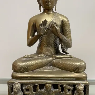 Sale Photo Thumbnail #65: Seated brass Buddha statue depicting the Dharmachakra mudra gesture, resting on an ornate pierced pedestal with carved figures.