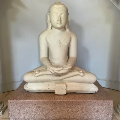 Sale Photo Thumbnail #16: Hand-carved white marble Jain Tirthankara statue depicted in a seated meditative pose, resting atop a rectangular reddish granite pedestal base.