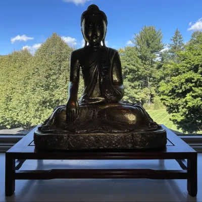 Sale Photo Thumbnail #66: Large seated bronze Buddha statue in the Bhumisparsha Mudra position, resting on a low wooden display stand.