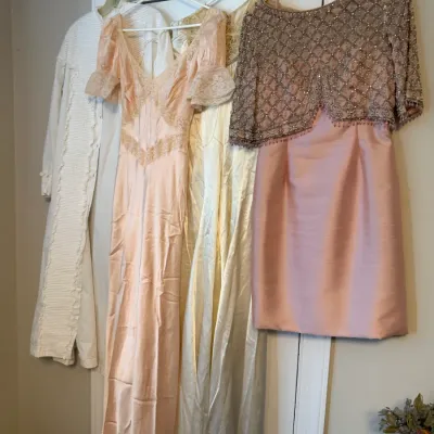 Sale Photo Thumbnail #132: Collection of vintage women's formal dresses and nightgowns, including a pink satin gown with lace detailing and a heavily beaded mid-century cocktail dress, hanging on a door frame.