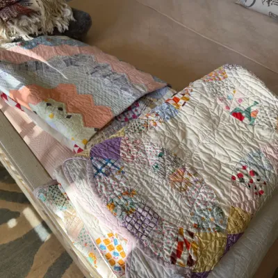 Sale Photo Thumbnail #175: Collection of handmade vintage quilts, including a double wedding ring pattern and chevron patchwork design, displayed alongside fringe throw blankets on a bed.
