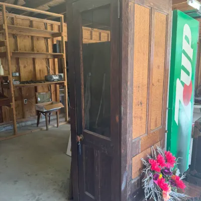 Sale Photo Thumbnail #198: Vintage wooden telephone booth featuring a glass-paneled door with a round knob, paneled side walls, and an original dark finish with visible wear.