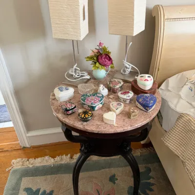 Sale Photo Thumbnail #187: Round pink marble-top side table with cabriole legs, featuring a collection of decorative trinket boxes, pair of modern tall rectangular lamps, and artificial floral arrangement.