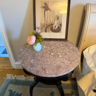 Sale Photo Thumbnail #130: Round side table featuring a pink mottled marble top and dark cabriole legs, topped with a small vase of faux flowers and a framed antique print.