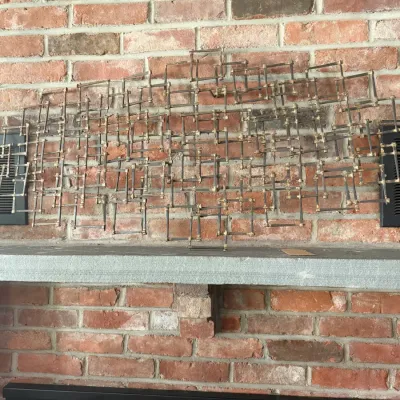 Sale Photo Thumbnail #227: Mid-century modern brutalist metal nail sculpture wall hanging, mounted above a brick fireplace mantle.