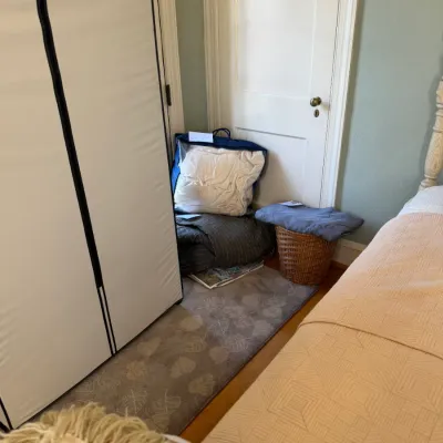 Sale Photo Thumbnail #174: Corner of a bedroom featuring a portable fabric wardrobe, a small patterned runner rug, a woven wicker basket, and bagged bedding.