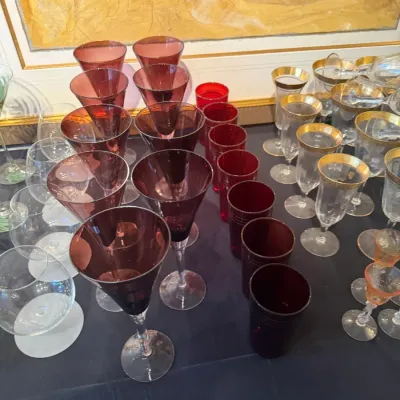 Sale Photo Thumbnail #161: Large assortment of vintage glassware, including deep red wine goblets with clear stems, ruby red tumblers, and gold-rimmed crystal stems.