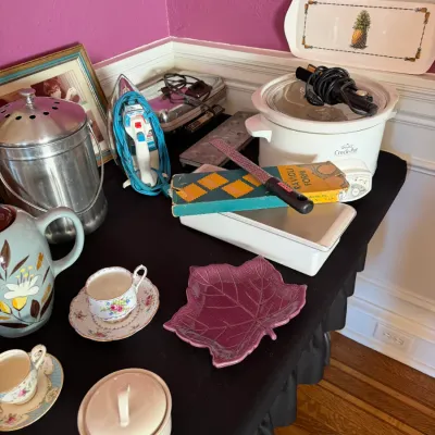 Sale Photo Thumbnail #110: Assortment of household wares and kitchen items, including a Rival Crock-Pot slow cooker, a vintage clothing iron, floral teacups, and a purple leaf-shaped dish.