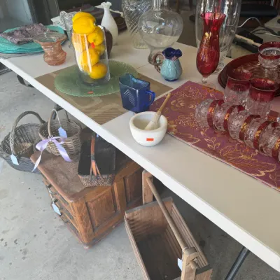 Sale Photo Thumbnail #208: Folding table displaying assorted glassware, decorative ceramics, and stemware alongside wooden caddies, baskets, and small furniture pieces below.