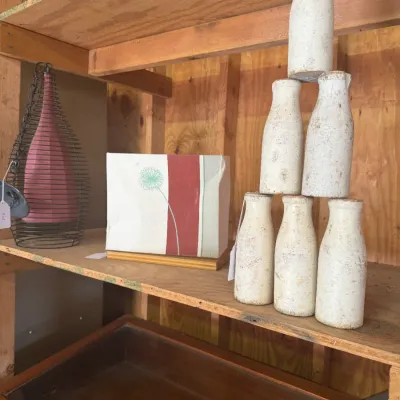 Sale Photo Thumbnail #202: Set of six distressed white milk bottle-shaped carnival game pins stacked on a wooden shelf alongside decorative home items.