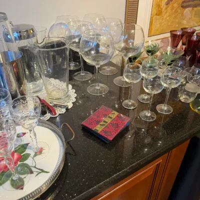 Sale Photo Thumbnail #159: Collection of glassware including balloon wine glasses, cordial stems, and a clear glass pitcher displayed on a dark countertop.