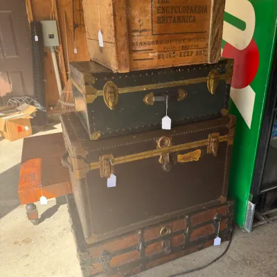 Sale Photo Thumbnail #200: Stack of vintage trunks and a wooden crate, including an embossed 'The Encyclopaedia Britannica' book shipping crate topped over several antique flat-top steamer trunks.