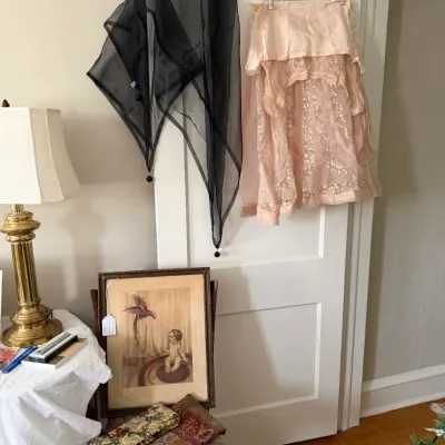 Sale Photo Thumbnail #182: Vintage sheer black scarf with beaded tassels and a delicate blush lace dress hanging from a door, alongside a brass table lamp and framed vintage artwork.