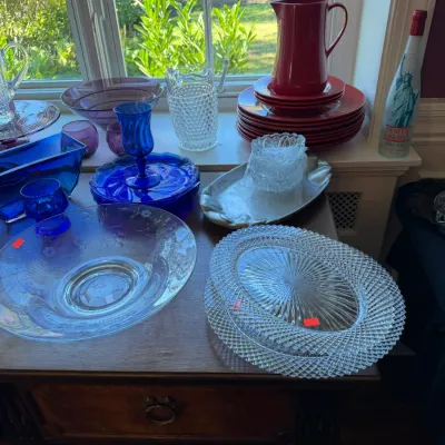 Sale Photo Thumbnail #102: Collection of glassware and tableware, including pressed cut-glass serving platters, cobalt blue glass stemware, an etched floral bowl, and a red ceramic pitcher with matching plates.
