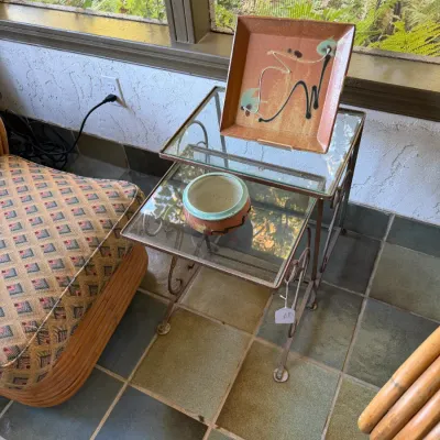Sale Photo Thumbnail #84: Set of two nesting metal and glass side tables featuring scrollwork details, holding decorative ceramic pieces including a square glazed tray.