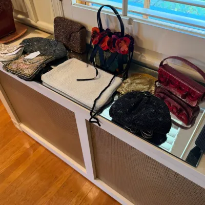 Sale Photo Thumbnail #167: Collection of vintage women's handbags and evening purses, including beaded, sequined, and faux-crocodile styles displayed on a mirrored top cabinet.
